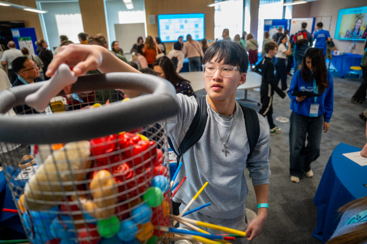 A boy is stood in a busy seminar room is dropping a toy bone into a basket