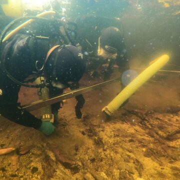 Two divers with equipment looking at the ocean floor.
